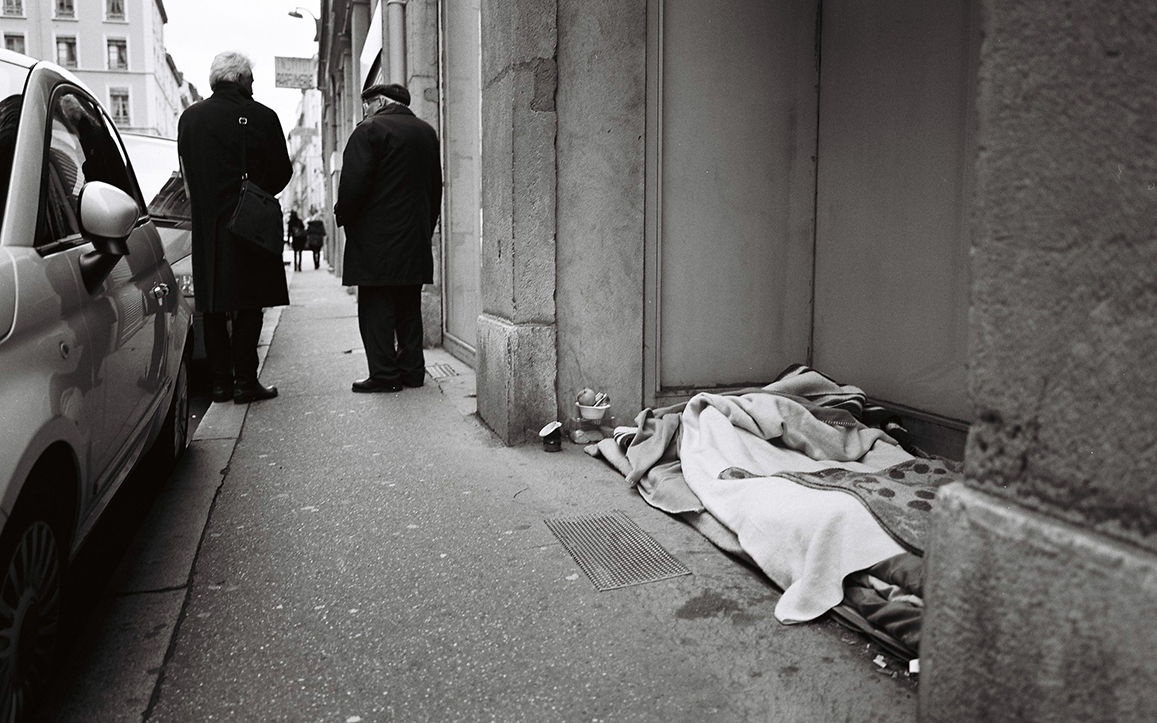 Photographie de rue montrant un matelas et quelques affaires appartenant à un SDF à Lyon, avec en perspective 2 hommes de dos discutant